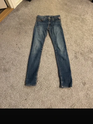 Blå skinny jeans från Replay - Snygga blå skinny jeans från Replay med klassisk femficksdesign och diskreta slitningar. Jeansen har låg midja och tydliga kontrastsömmar. Perfekta för dig som gillar en tight passform och stilren look.