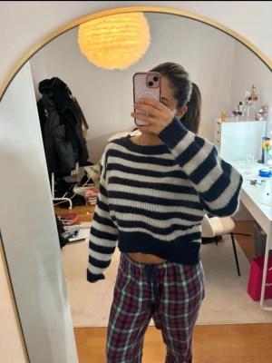 Randig stickad cropped tröja - Mysig stickad tröja med breda marinblå och vita ränder. Croppad modell med långa ärmar och rund halsringning. Perfekt för en avslappnad och trendig look. Materialet ser ut att vara mjukt och lite fluffigt.