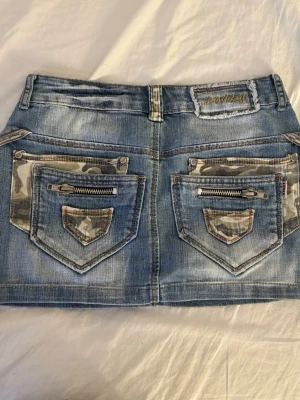 jeanskjol - Säljer en blå kort jeanskjol från Lonky med coola camouflage-detaljer på bakfickorna och dragkedjor. perfekt för sommaren. skriv för mer bilder/ frågor. pris kan diskuteras 😊
