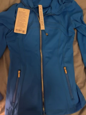  Lululemon kofta / träningsjacka 😝 - Vill få såld snabbt- kom med bud! Snygg blå zip hoodie från Lululemon med figurnära passform. Jackan har dragkedja framtill, två fickor med dragkedja och alla är i guldfärg. Perfekt till träning eller vardag. Tillverkad i stretchigt funktionsmaterial. Den är helt ny, med lapp kvar och påse. Säljer åt en vän, men kan alltid fixa fler bilder om det behövs. Hör av er vid frågor! Egna bilder!