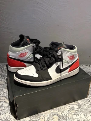 Nike Air Jordan 1 Mid svart/vit/röd - Säljer ett par Nike Air Jordan 1 Mid sneakers i svart, vitt och rött. Klassisk design med svart swoosh, röda detaljer vid hälen och vita paneler.               Riktigt snygga! I princip helt oanvända. Nypris ca 2900
