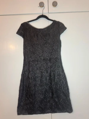 Svart spetsklänning med öppen rygg - Snygg svart och silvrig kortklänning med spetsdetaljer. Öppen rygg med knytband bak. Perfekt för utgång eller bara vara snygg🤩       Har endast testat den en gång köpt för 450kr🫶🏻