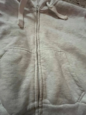 Ljusgrå zip-hoodie med fickor - Säljer en ljusgrå hoodie med dragkedja och huva med dragsko. Hoodien har två stora fickor framtill och ribbade muddar vid ärmslut och nederkant. Perfekt för en avslappnad och stilren look. Lite kortare än vissa hoodies men passar perfekt till många outfits! Den är köpt från Gina Tricot, hoodien har nån fläk någonstans men de går säkert bort i tvätten. Den är i storlek XS.