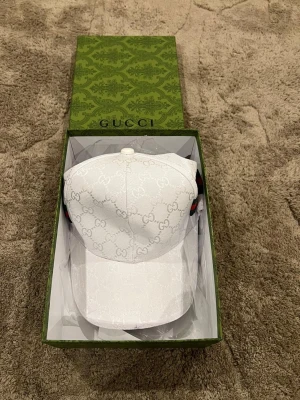 Beige keps med monogram - Säljer en beige keps med det klassiska monogrammönstret över hela plagget. Västen har en stilren och tidlös design som sticker ut med sitt exklusiva märke. Perfekt för dig som vill ha något unikt och trendigt i garderoben.