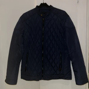 Mörkblå höstjacka Hunter Story L - Snygg mörkblå quiltad jacka från Hunter Story i storlek L. Jackan har dragkedja framtill, två fickor med dragkedja och ett stilrent rutmönster. Perfekt för dig som gillar en klassisk look med modern touch. 10/10 skick då jag typ inte använt den då den är för liten