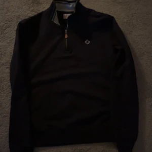 half zip tröja från Morris - Snygg svart långärmad tröja från Morris med half zip och liten broderad logga på bröstet. Perfekt för lager-på-lager och har en klassisk ståkrage. Passar dig som gillar stilrena och tidlösa plagg.