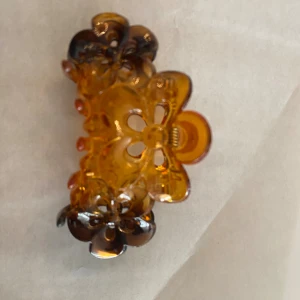 Brun hårklämma med blommor - Snygg hårklämma i transparent brun plast med blommönster och detaljer i mörkare nyans. Perfekt accessoar för att snabbt fixa frisyren och ge en söt touch till din look. Helt ny , finns fler och svart färg kvar eller 