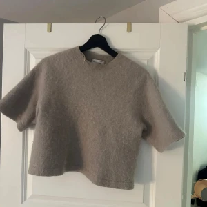 Beige stickad topp från & Other Stories - Supermjuk och croppad beige stickad topp från & Other Stories. Modellen har korta ärmar, rund halsringning och en enkel, stilren look. Perfekt för lager-på-lager och passar till både jeans och kjol.