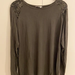 Mörkgrön långärmad topp med spets - Snygg mörkgrön långärmad topp med spetsdetaljer på axlarna. Rund halsringning och mjukt material som känns skönt mot huden. Extremt skönt matrial. Storlek L och är från Cubus.