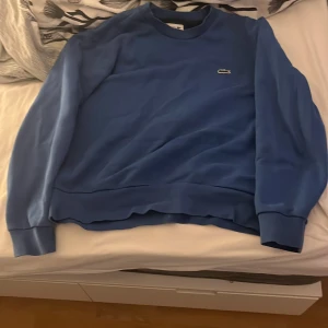 Blå sweatshirt från Lacoste i bomull - Säljer en blå crewneck sweatshirt från Lacoste i klassisk passform. OBS!!! Det står att den är M men den sitter som S, alltså är den S. Priset går såklart att förhandla ✌️