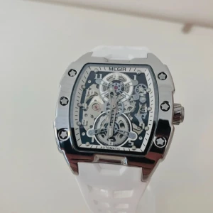 MEGIR automatisk klocka med vit rem - Snygg automatisk klocka från MEGIR med rektangulärt skeletturverk och detaljerad urtavla. Klockan har en robust boett i silverfärgad metall och en sportig vit silikonrem. Genomskinlig baksida visar det mekaniska urverket.                                                                                          ✅Helt Ny✨.                                                                                    ✅Frakt inom 24 timmar📦.                                                      ✅Kommer med Låda 🗃️