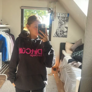 Svart hoodie D1rCüt San Diego L - Svart hoodie från D1rCüt San Diego med stor rosa logga framtill. Storleken är L men passa mig som är S