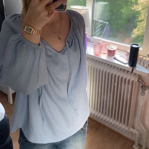 Ljusblå blus med knyt i halsen - Säljer en luftig ljusblå blus med trekvartsärmar och knytband i halsen. Blusen har en lätt textur i tyget och en avslappnad passform som ger en skön känsla. Perfekt att styla med jeans eller kjol för en fräsch look. Använt 2 ggr