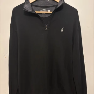 Svart half zip tröja Polo Ralph Lauren - Svart långärmad tröja från Polo Ralph Lauren med klassisk grå logga på bröstet. Tröjan har en snygg half zip-dragkedja och hög krage med grå insida. Perfekt som övertröja nu till hösten/vintern. Tröjan har blivit använd max 4 gånger men inte blivit använd något mer på grund av att den är lite för stor. Storleken är M men jag skulle säga att den passar L bra då den är lite lång i armarna. Den har inte det minsta täcken på användning eller några som helst slitage. Om du överväger så hör av dig!