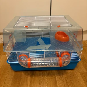 Hamsterbur med rör och tillbehör 3 våningar  - Praktisk hamsterbur med plasttunnel, hjul, ramp och matskål. Buren är rymlig och har god ventilation. Viss rost och slitage syns på gallret (se bild), men i övrigt i bra skick. Perfekt för små gnagare som behöver aktivitet och trygghet. 