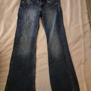 Low waist bootcut jeans blå - Klassiska low waist jeans i blå denim med bootcut passform. Snyggt slitna detaljer framtill och femficksmodell. Jeansen har normal midja och är tillverkade i robust bomullsjeans. Perfekta för dig som gillar retrovibbar och bredare ben.