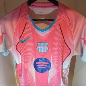 FC Barcelona rosa matchtröja Nike S - Säljer en FC Barcelona fotbollströja från Nike i rosa och blått med klubbmärke och Spotify-logga på bröstet. Tröjan är kortärmad, tillverkad i Dri-FIT-material och har grafiska linjer och detaljer i vitt och blått. Perfekt för dig som vill sticka ut på planen.