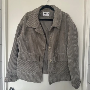 Beige manchesterjacka från NA-KD M - Säljer en beige manchesterjacka från NA-KD med breda ribbor och stora fickor framtill. Jackan har klassisk krage, knäppning med knappar och långa ärmar med knappdetaljer vid ärmslut. Perfekt för dig som gillar en chill och trendig look.