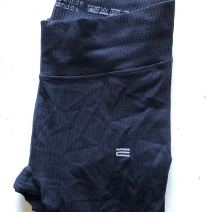 Svarta träningstights från Endurance - Svarta tights från Endurance med hög midja och diskret logga framtill. Tillverkade i stretchigt material (92% polyamid, 8% spandex) som sitter tight och bekvämt. Perfekta för gymmet eller löprundan, med ribbad midja för extra stöd.