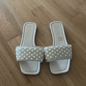 Vita sandaler med pärlor och glitter - Snygga vita sandaler med fyrkantig tå och bred rem dekorerad med pärlor och glitter. Platt sula och öppen tå, perfekt för sommarens alla tillfällen. Tillverkade i syntetmaterial med svart undersula för extra grepp. Använda 1 gång storlek 37 