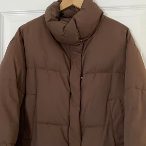 Brun pufferjacka från Bershka - Säljer en brun pufferjacka från Bershka i storlek S. Jackan har hög krage, två fickor framtill och stängs med tryckknappar. Perfekt för kalla dagar och har en riktigt skön, oversized känsla.