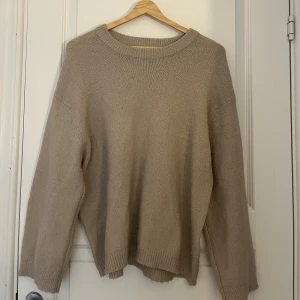 Beige stickad tröja med rund hals - Säljer en enkel och snygg beige stickad tröja med rund hals och långa ärmar. Tröjan har en loose passform och ribbade muddar vid hals, ärmslut och nederkant. Perfekt för att hålla sig varm och se chill ut under kyliga dagar.