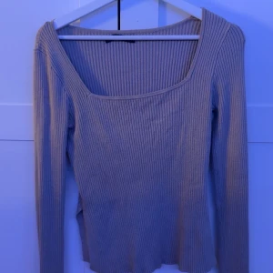 Beige ribbad långärmad topp - Snygg beige ribbad topp med lång ärm och fyrkantig ringning. Toppen har  liten slits på båda sidorna och är tillverkad i ett stretchigt material som sitter skönt på kroppen. Perfekt att styla med jeans eller kjol för en clean look.