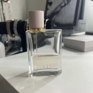 Burberry parfym i stilren flaska - Säljer en Burberry parfym i en elegant, genomskinlig glasflaska med diskret guld-detalj vid halsen och ljusgrått lock. Flaskan har en modern, fyrkantig form och Burberry-loggan ingraverad framtill. Perfekt för dig som gillar klassisk och lyxig doft.