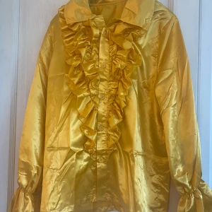 Gul-guldig satinskjorta till ex 70-talsfesten?  - Min man köpte den nyligen ( webbsida Partykungen)  för att använda på ett 70-talsfest! Den gjorde succé ihop med svarta utsvängda byxor ( se min andra annons)  skjorta nypris: 300kr