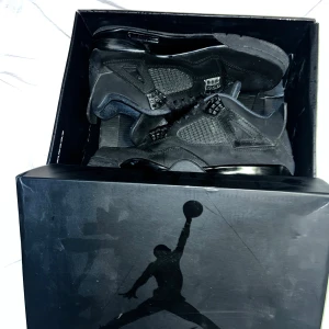 Svarta Nike Air Jordan 4 Retro - Säljer ett par svarta Nike Air Jordan 4 Retro med klassisk mesh och detaljer i mocka. Skorna har snörning, ikonisk Jumpman-logga på plösen och hälen samt en chunky sula. Perfekta för dig som gillar streetwear och vill ha en stilren sneaker med mycket attityd.
