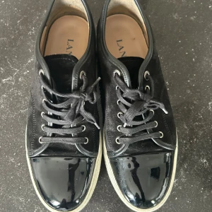 Svarta sneakers från Lanvin med lackad tå - Säljer dessa jätte fina Lanvin. De är äkta och kvittot finns. Använda fåtal gånger och är köpta förra året, jättebra skick. De är i storlek 9 vilket motsvarar 43/44. Säljer för att de är lite för små för min kille