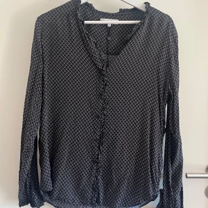 Marinblå rutig blus  - Marinblå rutig blus. Mönstret är rutor med prickar i där rutorna är linjerade med vit. Blusen har bolaget längs krage och ärmhål 