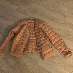 Gammelrosa dunjacka från Uniqlo S - Supersmidig och lätt dunjacka från Uniqlo i en rosa nyans. Jackan är quiltad, har rund halsringning och knäpps med tryckknappar framtill. Perfekt för lager-på-lager och enkel att ta med sig tack vare sin ultralätta design.