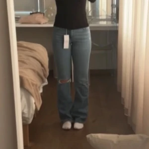Blå lowwaist bootcut jeans med hål i ena knät - Säljer mina älskade jeans från Gina som tyvärr har blivit för små. De finns inte att köpa längre och är väldigt populära. Knappt använda och därför i bra skick, storlek 34🥰