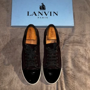Lanvin sneakers i vinröd mocka - Säljer ett par stilrena Lanvin sneakers i vinröd mocka med svart lackad tå och vita sulor. Skorna har svarta skosnören och klassisk låg profil. Perfekta för dig som vill ha en lyxig och clean look med exklusiv känsla. PRIS KAN DISKUTERAS!