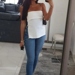 Vit bandeau tubtopp med dragkedja från zara - Säljer en stilren vit bandeau tubtopp med snygg asymmetrisk kant och dragkedjedetalj i sidan. Toppen är axelbandslös och har en clean, modern look som passar perfekt till jeans eller kjol. Materialet känns slätt och lätt, perfekt för varmare dagar.