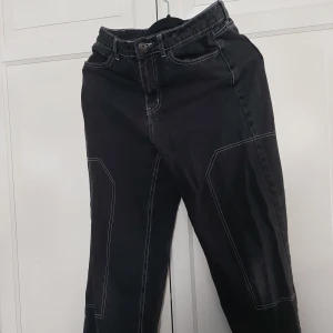 Svarta jeansbyxor med kontrastsömmar - ⚠️ Skriv till mig innan köp!⚠️Svarta jeansbyxor med vita kontrastsömmar och coola detaljer på benen. Modellen har raka ben och klassiska fickor både fram och bak. Materialet är jeans och passformen är normal. Perfekt för dig som gillar streetstyle och vill sticka ut lite extra.