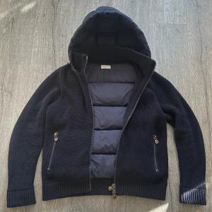 Moncler cardigan  - Snygg mörkblå cardigan jacka från Moncler med stickade ärmar och quiltad front och rygg. Jackan har huva, två dragkedjefickor och Moncler-logga på ärmen. Perfekt för kyliga dagar och ger en clean, sportig vibe. Nyskick men en gammal moncler modell. Inga defekter.