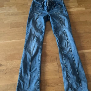 Blå jeans med raka ben och fickor - Säljer ett par ljusblå jeans med raka ben och markerade sömmar framtill. Jeansen har två stora fickor med lock och dragkedja framtill samt klassiska bakfickor. Snygg tvätt och coola detaljer, perfekt till en avslappnad stil.