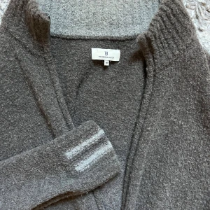 Grå kofta från Hansen & Jacob  - Mysig grå/brun kofta från Hansen & Jacob i storlek M. Koftan är i cashmere och har dragkedja framtill och ribbade muddar. Ärmarna har två ljusare ränder vid mudden för en detaljerad och stilren look. Perfekt nu till hösten!