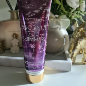 Victoria's Secret Coconut Sol Shimmer - Glittrande kroppslotion med kokosdoft från Victoria's Secret. Tuben är lila med guldiga detaljer och innehåller 236 ml. Ger huden en skimrande finish och doftar av kokos, mexikansk solros och havsbris. Perfekt för dig som vill ha glow och tropisk känsla. Helt ny och oanvänd svarar ej på bud