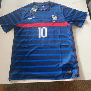 Frankrike Mbappé #10 Nike fotbollströja - Snygg blå fotbollströja  med Frankrikes landslagsmärke, nummer 10 och Mbappé på ryggen. Tröjan har horisontella ränder i olika blå nyanser och en röd detalj över bröstet. Tillverkad i lätt och ventilerande material, perfekt för match eller träning.