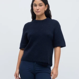 Mörkblå stickad kortärmad tröja - Mysig mörkblå stickad tröja med korta ärmar och rund hals. Tröjan har en enkel och stilren design, perfekt för lager-på-lager och funkar året runt. Materialet är fluffigt och ger en soft känsla. Passformen är normal och tröjan slutar vid höften.