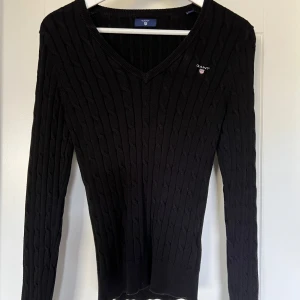 Svart kabelstickad tröja - Svart kabelstickad tröja från Gant med v-ringning och diskret logga på bröstet. Använd fåtal gånger. 
