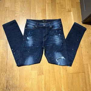 Mörkblå skinny jeans Supply & Demand - Mörkblå skinny jeans från Supply & Demand med slitningar och färgstänk för en bättre look. Klassisk men väldigt feta köpte dom för 2000 kr men väljer att sälja dom billigt för snabb affär och vill bli av med dom. Inte slitna och passar som normala byxor inte bara skinny.