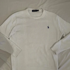 Vit stickad tröja från Polo Ralph Lauren - Vit stickad tröja från Polo Ralph Lauren med klassisk rund halsringning och broderad marinblå logga på bröstet. Tröjan har ribbade muddar vid ärmslut och nederkant, perfekt för en clean och stilren look.                                                                                  Tja, säljer denna feta Polo Ralph Lauren tröjan. Använd några gånger men inga defekter förutom i kragen !!se sista bild!! 