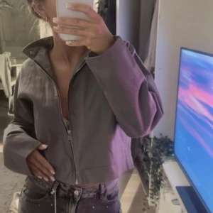 Grå jacka  - Snygg grå jacka med prislappar kvar och med dragkedja framtill och bred krage med tryckknappar. Jackan har långa ärmar och en loose fit, perfekt för dig som gillar en avslappnad stil. Tillverkad i bomullsmaterial som känns skönt mot huden.