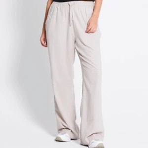 Beiga vida linnebyxor!  - Snygga och avslappnade beiga linnebyxor med bred passform och resår i midjan samt snörning. Byxorna har raka, vida ben och är perfekta för en chill och stilren look. Lätta och luftiga i materialet. Byxorna har en ficka där bak på ena sidan (porto tillkommer). 