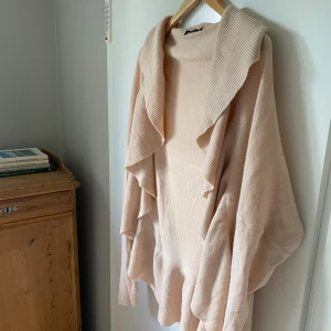 Ljusrosa kofta med volang från Gina Tricot - Supersöt ljusrosa kofta från Gina Tricot med volangkant längs hela öppningen och nederkanten. Koftan är stickad, har lång ärm och en oversized, loose passform. Perfekt att slänga över en topp för en chill och trendig look.