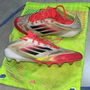 Adidas F50 fotbollsskor röd/gul 43⅓ - Säljer ett par Adidas F50 fotbollsskor i storlek 43⅓. Skorna har en snygg mix av rött, gult och vitt med svarta Adidas-ränder. Lätta och smidiga med snörning och platt sula med dobbar för gräsplan. Perfekta för dig som vill sticka ut på planen. Jättebra skick lite smutsiga bara annars skit bra skor och väger inget och man känner sig mycket snabbare 